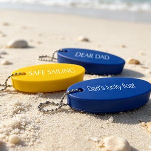 May include: Three oval-shaped foam key floats with metal ball chains. One yellow float is printed with "SAFE SAILING" in white. Two blue floats are printed with "DEAR DAD" and "Dad's lucky float" in white text, respectively.