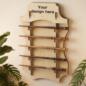 May include: A light-colored wooden wall-mounted display rack featuring five horizontal slots for holding wands. The top section of the rack has the text Your design here printed in black. The rack has a decorative, curved silhouette.