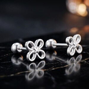 May include: A pair of silver-toned stud earrings featuring a four-petaled openwork flower design with a small cross detail at the center. Each earring has a straight post and a round ball backing, showcasing a polished metallic finish throughout.