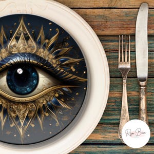 May include: A white-rimmed plate with a dark blue eye design, gold and blue accents, and a silver fork and knife. The plate features a detailed eye illustration. The fork and knife have ornate handles. The plate is on a wooden surface.