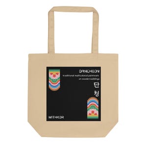 May include: A beige tote bag featuring a black square graphic with colorful Dancheon patterns, the text "Dancheon traditional multicolored paintwork on wooden buildings," Korean characters, and the brand name "WITHKOR" printed on the front.