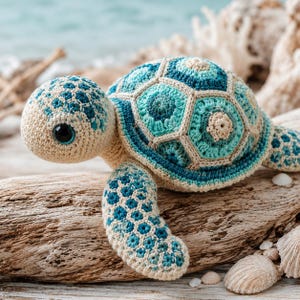 Puede incluir: Un peluche de tortuga marina tejido a ganchillo con cabeza y aletas de color crema con detalles en azul y turquesa. El caparazón está formado por parches hexagonales en varios tonos de azul, turquesa y crema, con un gran ojo negro.