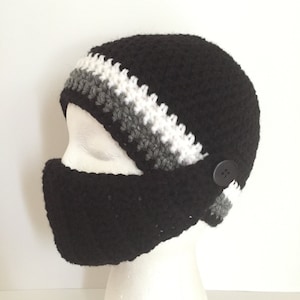 May include: Black crocheted beanie with a grey, white and black striped band. The beanie has a button on the side and a matching black face mask.