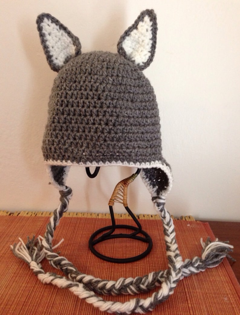 May include: Gray crocheted hat with white crocheted ears and a long white and gray braided cord.
