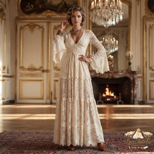 Peut inclure: Une robe longue en dentelle couleur crème dotée d'un décolleté en V profond, de longues manches évasées et d'une jupe à étages. Le vêtement est confectionné dans une dentelle florale complexe avec un corsage ajusté et une silhouette fluide.