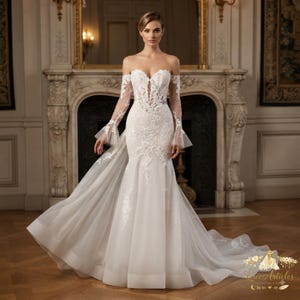 Peut inclure: Une robe de mariée ivoire à épaules dénudées avec un décolleté en cœur, des manches longues transparentes à poignets évasés et un corsage ajusté orné de broderies florales blanches complexes se prolongeant sur une jupe en tulle fluide.