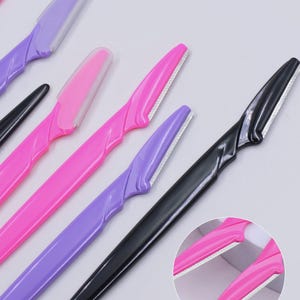 May include: A collection of facial razors in black, purple, and pink, each featuring a long plastic handle and a single blade with a protective plastic cover. A circular inset shows a close-up view of two pink razors with their blades exposed.