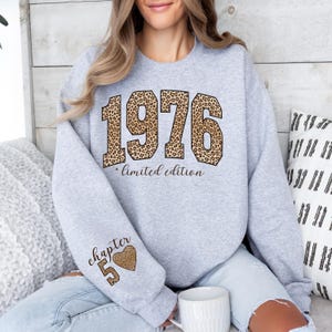 May include: A light gray crewneck sweatshirt featuring the number 1976 in a brown and black leopard print pattern, with the text "limited edition" below it. The sleeve displays the text "chapter 50" next to a leopard print heart icon.