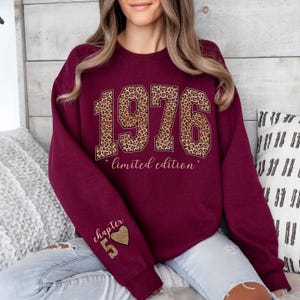 May include: A maroon crewneck sweatshirt featuring the year 1976 in a large leopard print font across the chest, with the text "limited edition" below it. The left sleeve displays the text "chapter 5" above a small leopard print heart and the number 5.