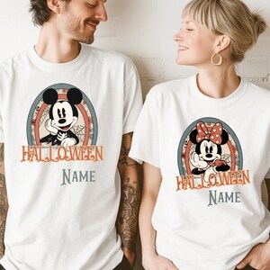 May include: Two white crew neck t-shirts featuring a vintage-style graphic of Mickey Mouse and Minnie Mouse in Halloween costumes. Each shirt displays the word HALLOWEEN in orange text above the word NAME in grey, set within a circular frame.