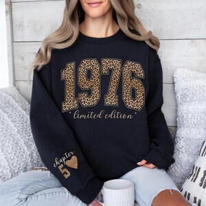 May include: A black crewneck sweatshirt featuring the text 1976 in a brown and black leopard print pattern, with the words limited edition printed below. The left sleeve displays the text chapter 5 with a small leopard print heart icon.