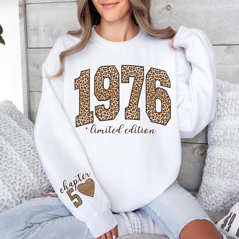 May include: A white long-sleeve sweatshirt featuring the large brown and black leopard print numbers 1976 centered on the chest, with the text limited edition below. The right sleeve displays the text chapter 50 with a leopard print heart.