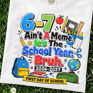 May include: A white t-shirt featuring a colorful graphic with the text 6-7 Ain't A Meme. It's The School Year. Bruh. 2026-2027 FIRST DAY OF SCHOOL. The design includes illustrations of a blue backpack, books, a globe, pencils, and school supplies.