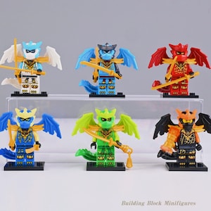 Puede incluir: Seis minifiguras de bloques de construcción dispuestas en dos filas, cada una con alas de dragón, una máscara y una espada. Las figuras son de colores blanco y azul, azul oscuro, rojo, azul claro, verde, y negro y naranja, sobre bases negras.
