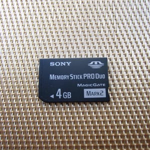 May include: A black Sony Memory Stick PRO Duo flash memory card with 4GB capacity. The card features white text reading SONY, MEMORY STICK PRO DUO, MAGICGATE, 4 GB, and MARK2, along with a white logo in the upper right corner and a small arrow icon.