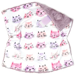 May include: A white baby blanket featuring a repeating pattern of watercolor cat faces in shades of pink, purple, and peach. The blanket has a soft, plush, gray border and a matching ribbon.