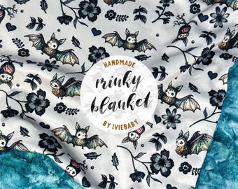 May include: A handmade minky blanket with a white background featuring a pattern of bats, flowers, and hearts in black and teal. The blanket has a teal plush backing and the text "handmade minky blanket by IVIEBABY".