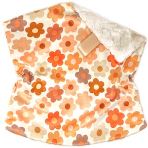 May include: A baby blanket with a floral pattern in shades of orange, brown, and cream. The blanket has a soft, plush backing and a satin ribbon. The blanket is designed with a retro flower power theme.