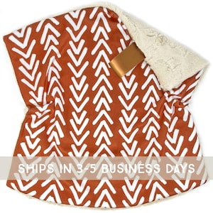 May include: A soft, reversible blanket with a rust-colored chevron pattern on one side and a cream-colored plush material on the other. A gold-colored ribbon is attached to the blanket. The text "SHIPS IN 3-5 BUSINESS DAYS" is printed on the blanket.