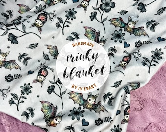 May include: A white minky blanket with a repeating pattern of bats, flowers, and leaves in shades of green, brown, and black. The blanket has a pink, textured backing. The text "HANDMADE minky blanket BY IVIEBABY" is in a circular design.