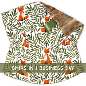 May include: A soft, plush blanket with a faux fur backing. The front features a white background with a repeating pattern of green leaves and orange foxes. The text "SHIPS IN 1 BUSINESS DAY" is printed on the bottom of the blanket.