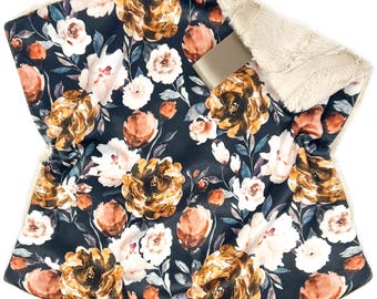 May include: A baby blanket with a floral pattern in shades of brown, peach, and white on a dark background. The blanket has a soft, cream-colored, plush backing and a satin ribbon.