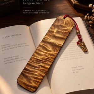 Puede incluir: Un marcapáginas rectangular de madera de Jinsi Nanmu con un patrón de veta Longdan ondulado. El marcapáginas cuenta con una borla de cordón rojo sujeta a través de un orificio en la parte superior, adornada con cuentas rojas y un dije metálico.
