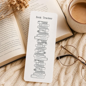 Puede incluir: Un marcapáginas rectangular blanco con un dibujo de líneas negras de una pila alta de libros y el texto Book Tracker impreso en la parte superior. El marcapáginas tiene un acabado liso y muestra una disposición vertical de libros.