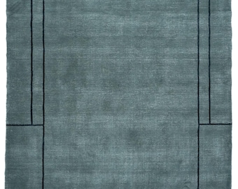 May include: A rectangular area rug in a solid slate blue color featuring a dark charcoal geometric border design. The pattern consists of a central rectangular frame with thin vertical lines extending from the top and bottom edges to the rug's border.