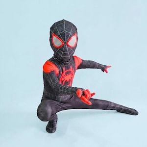 May include: A black and red Spider-Man costume with a web pattern, red accents, and a spider emblem on the chest. The costume includes a mask with white eye lenses and red trim. The person is in a crouching pose with one leg extended.