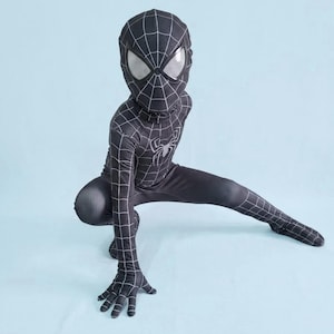 May include: A black Spider-Man costume featuring a web design and a spider emblem. The all-in-one suit includes a mask with white eye lenses. The person is in a crouching pose against a light blue backdrop.