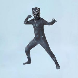 Può includere: Una tuta intera nera che riproduce un costume da supereroe con dettagli argentati e una maschera abbinata che copre l'intera testa. Il costume presenta maniche lunghe e pantaloni lunghi, con un motivo testurizzato sul petto e sugli arti.