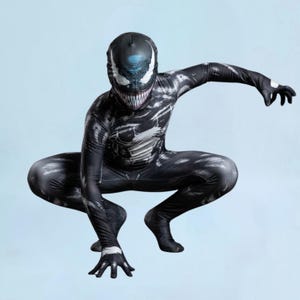 May include: A full-body black and white spandex bodysuit featuring a printed graphic of a creature with a wide, toothy grin and large white eyes. The suit covers the head, torso, arms, and legs, displaying a textured, mottled pattern throughout.