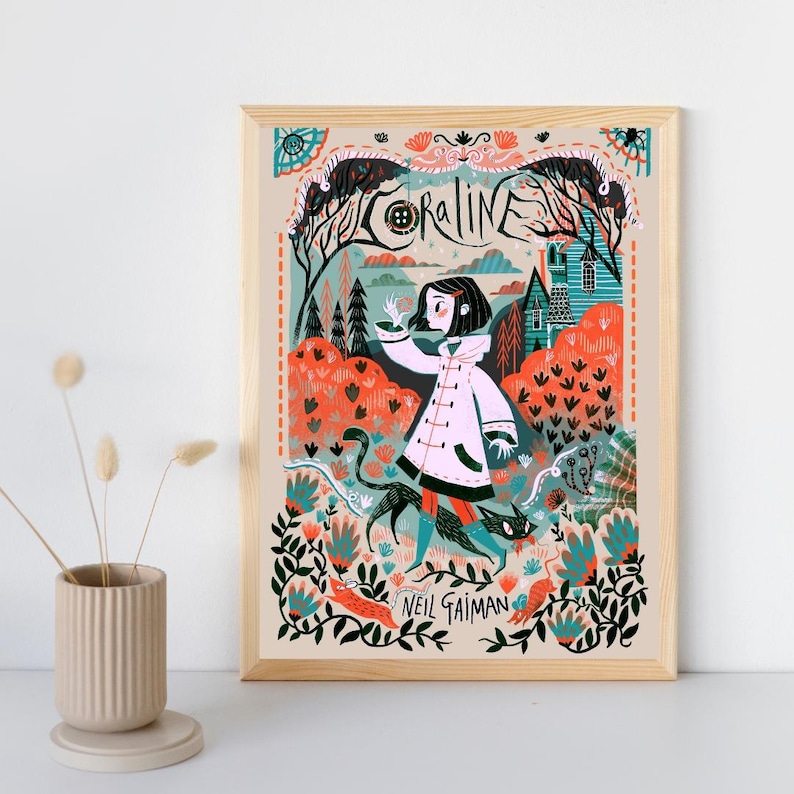 May include: A framed art print featuring a stylized illustration of Coraline with a black cat in a forest setting. The artwork includes the text Coraline and Neil Gaiman, with a color palette of orange, teal, black, and white, set in a light wood frame.