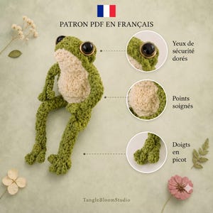 May include: A green crocheted frog toy with a cream-coloured belly and large black eyes with gold rims. The image includes text labels pointing to details: Yeux de s&eacute;curit&eacute; dor&eacute;s, Points soign&eacute;s, and Doigts en picot, plus TangleBloomStudio.