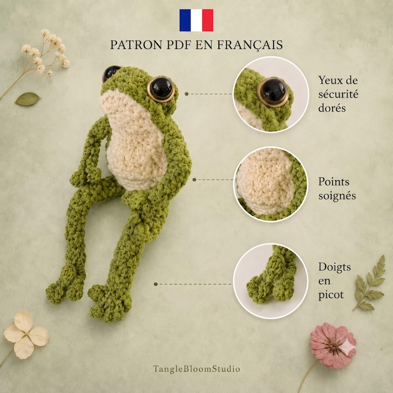 May include: A green crocheted frog toy with a cream-coloured belly and large black eyes with gold rims. The image includes text labels pointing to details: Yeux de s&eacute;curit&eacute; dor&eacute;s, Points soign&eacute;s, and Doigts en picot, plus TangleBloomStudio.