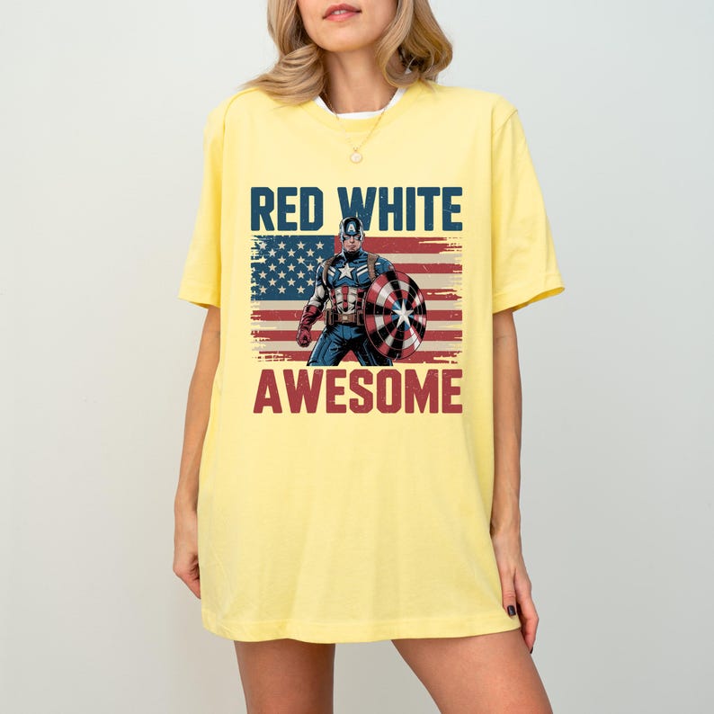 May include: A pale yellow short-sleeve t-shirt featuring a graphic print of Captain America holding a shield in front of a distressed American flag. The text RED WHITE AWESOME is printed in bold blue and red letters above and below the graphic.