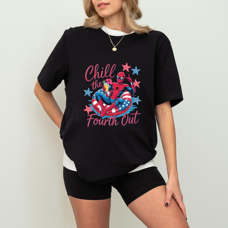 May include: A black short-sleeved t-shirt featuring a graphic of a superhero in a red and blue suit relaxing in a red, white, and blue striped pool float. The text Chill the Fourth Out is printed in pink, surrounded by red and blue star icons.