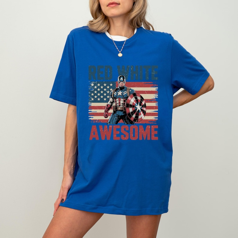 May include: A royal blue short-sleeve t-shirt featuring a graphic of Captain America holding a shield in front of a distressed American flag. The text "RED WHITE" appears above the character and "AWESOME" is printed in red below the graphic.