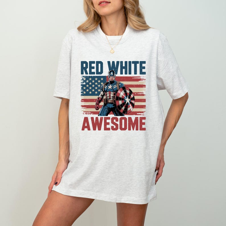 May include: A light heather gray short-sleeve t-shirt featuring a graphic of Captain America holding a shield in front of a distressed American flag. The text RED WHITE is printed in blue above the graphic, and AWESOME is printed in red below.