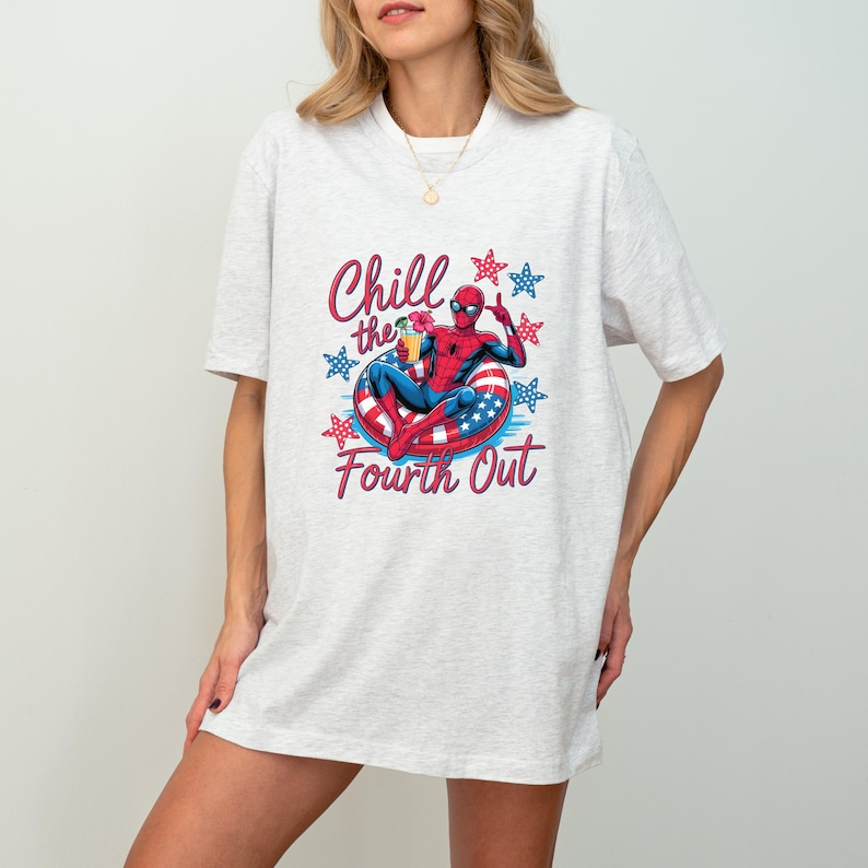 May include: A light heather grey t-shirt featuring a graphic of a superhero in a red and blue suit sitting on a red, white, and blue striped pool float. The text reads Chill the Fourth Out, surrounded by red and blue stars on the shirt front.