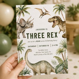 K&ouml;nnte beinhalten: Eine rechteckige Geburtstagseinladungskarte mit Aquarellillustrationen eines Triceratops, eines Pterodactyls, eines Tyrannosaurus Rex und eines langhalsigen Dinosauriers zwischen Palmen. Der Text lautet: JACKSON IS THREE REX, Join us for a ROAR-some 3rd Birthday Party, SATURDAY | OCTOBER 18 | 2-4 PM, The Miller Home, 456 Dino Trail, Austin, TX, RSVP to Emily at 555-238-4412.