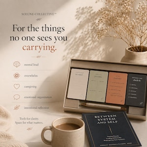 May include: A set of cards with the text "my mind", "priorities", "reminder", and "check-in" in a gray box. A pen and a book titled "Between System and Self" are also present. The image also includes a mug of coffee and a vase with dried flowers.