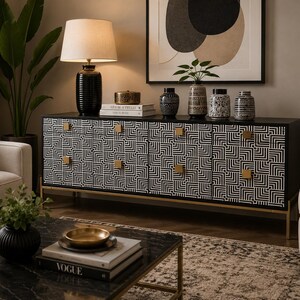 Peut inclure: Un long buffet noir doté de quatre portes d'armoire avec un motif géométrique blanc en labyrinthe et des poignées carrées dorées. Le buffet repose sur de fins pieds dorés et est surmonté d'une lampe de table noire et quatre vases en céramique.