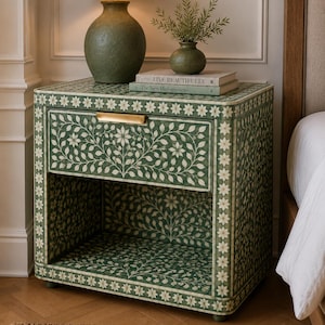 May include: A rectangular bedside table featuring a green and white floral inlay pattern with a repeating star border. The piece includes one drawer with a horizontal gold handle and an open storage shelf below, all finished in a smooth, patterned surface.