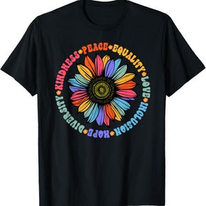 May include: A black short-sleeved t-shirt featuring a central graphic of a multi-coloured sunflower. Surrounding the flower in a circular pattern is the text: KINDNESS, PEACE, EQUALITY, LOVE, INCLUSION, HOPE, and DIVERSITY, separated by small flower icons.