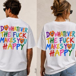 Può includere: Una t-shirt bianca a maniche corte con il testo multicolore DO WHATEVER THE FUCK MAKES YOU HAPPY stampato sul retro. Il design include due facce a forma di cuore arancione con espressioni sorridenti integrate nelle lettere.