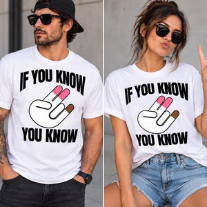 May include: A white short-sleeved t-shirt featuring the black text IF YOU KNOW YOU KNOW and a graphic of a hand making a two-fingered gesture with pink and brown colored tips. The design is centered on the chest of the garment.