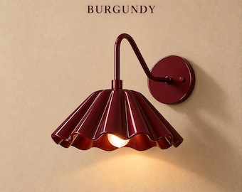 May include: A burgundy wall lamp featuring a scalloped, fluted shade and a curved metal arm attached to a circular wall mount. The word BURGUNDY is printed above the fixture, which emits a warm, glowing light from a central bulb.