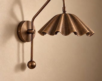 May include: A wall-mounted lamp with an antique bronze finish, featuring a circular base, a curved arm, and a downward-facing, scalloped, fluted shade. A vertical rod extends downwards from the arm, ending in a spherical weight.